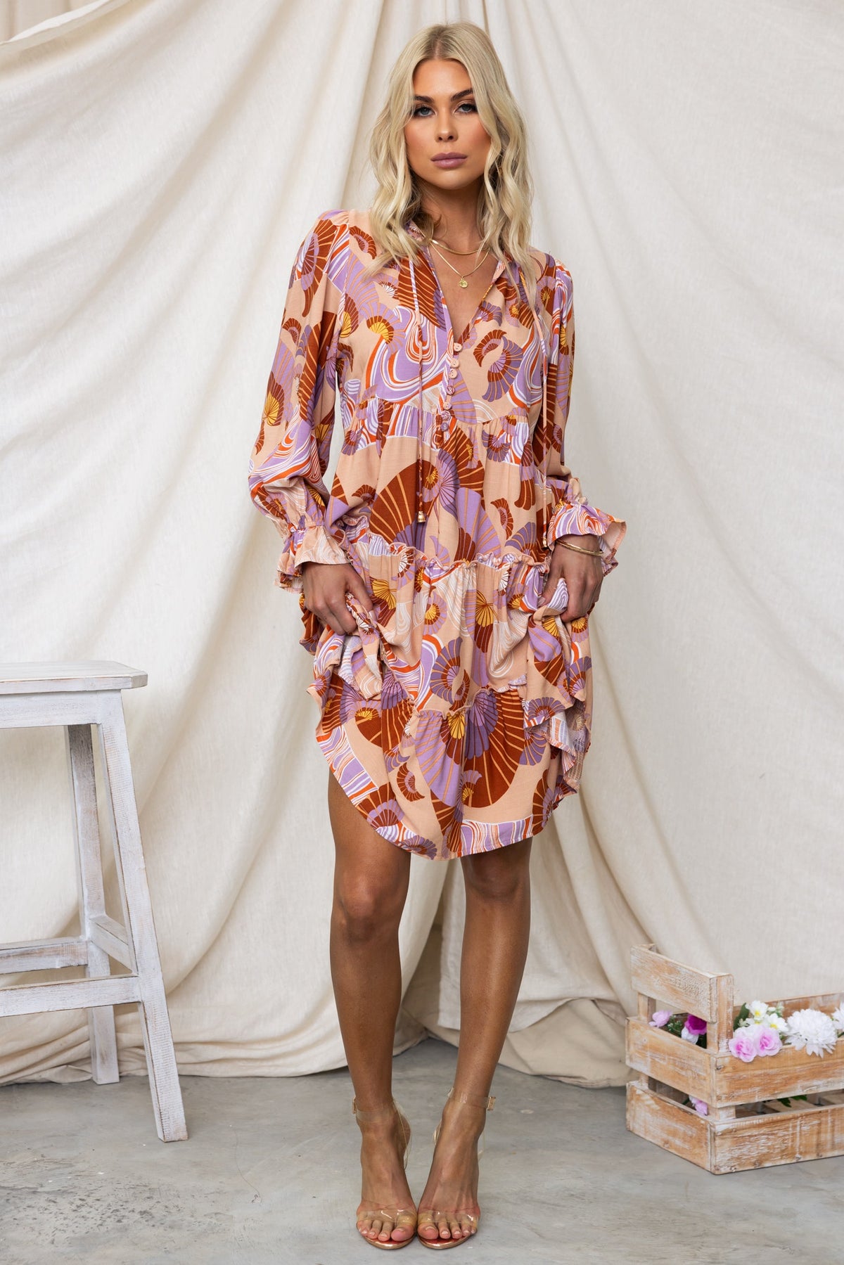 Model wearing the Boone Dress featuring a V-neckline, tie detail, ruffled layers, and floral print against a neutral backdrop.