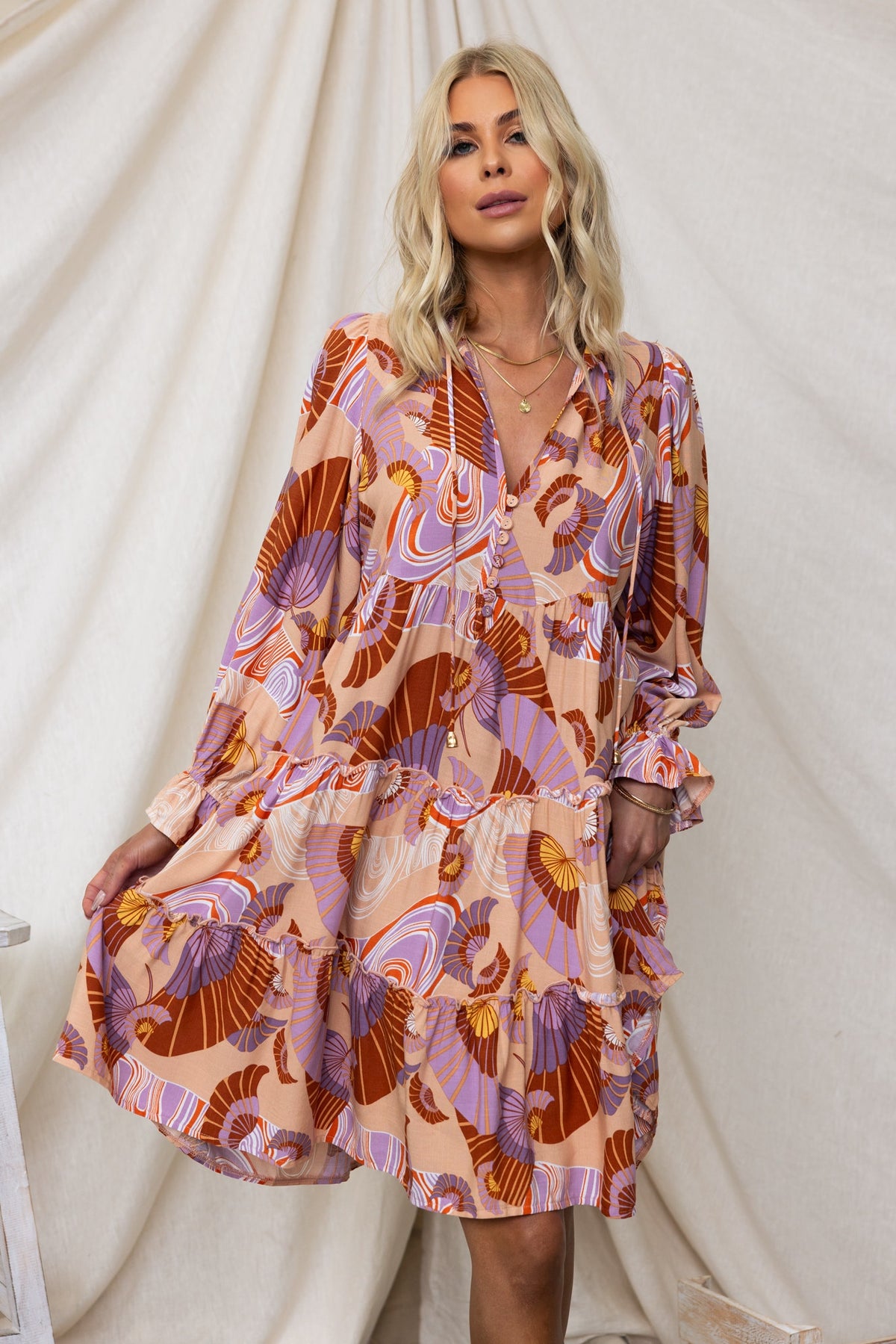 Model wearing the Boone Dress with a V-neckline and colorful swirl pattern, featuring a relaxed fit and tiered ruffles.