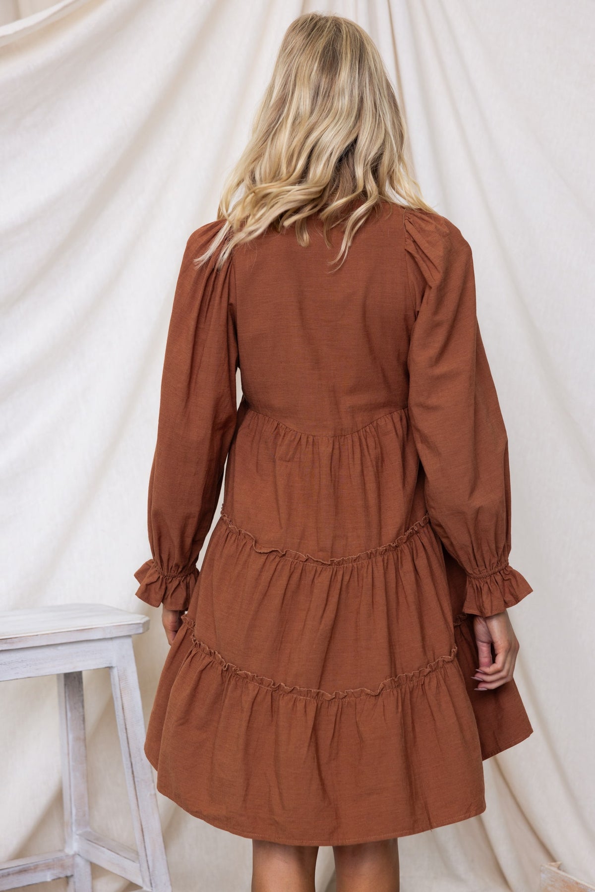 Back view of Boone Dress, featuring a tiered design and elastic sleeves in a warm brown color.