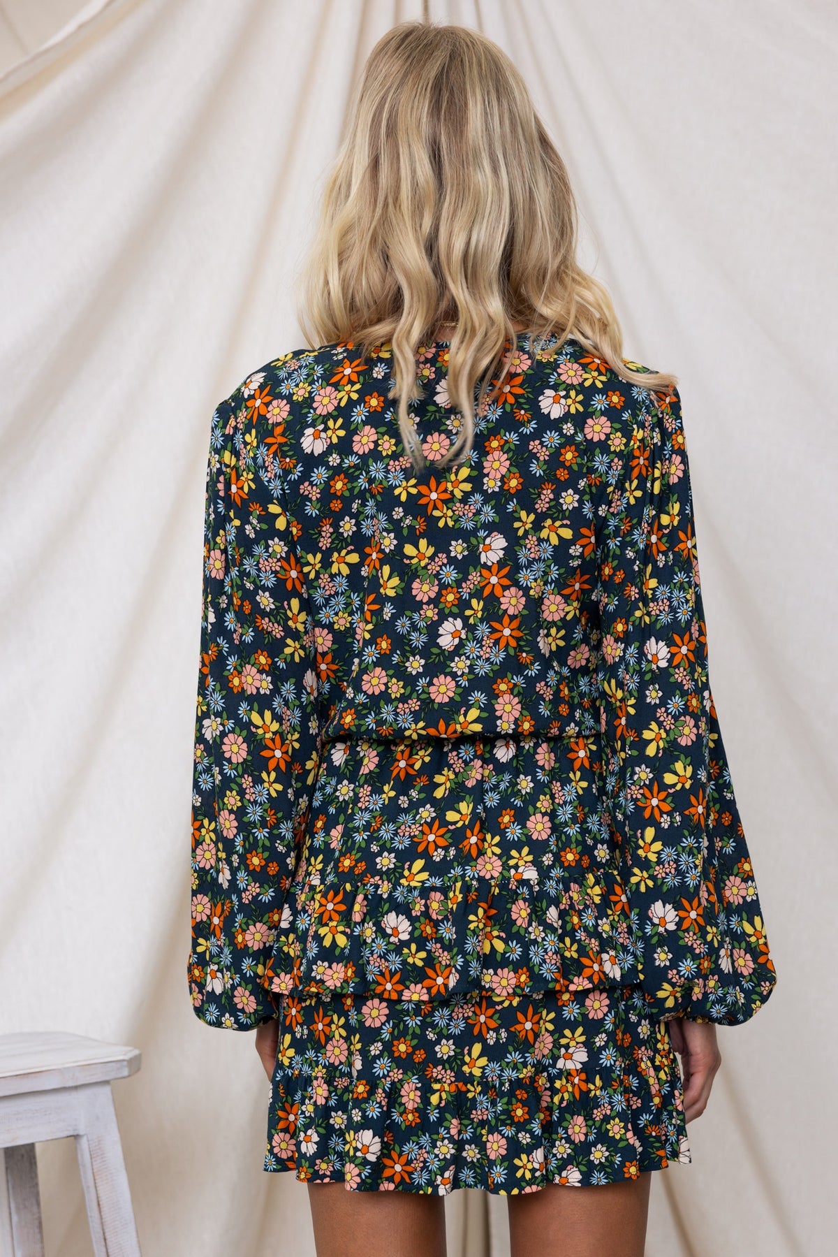 Back view of a floral Lanter Dress with long sleeves and ruffled hem, featuring a navy background with colorful flowers.