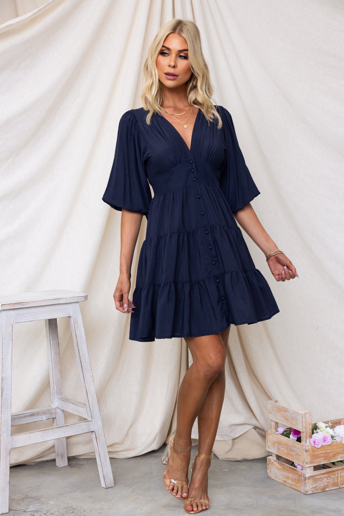 Navy Damika Dress with V-neckline, button-up front, and drawstring tie at sleeves, styled with a relaxed fit.
