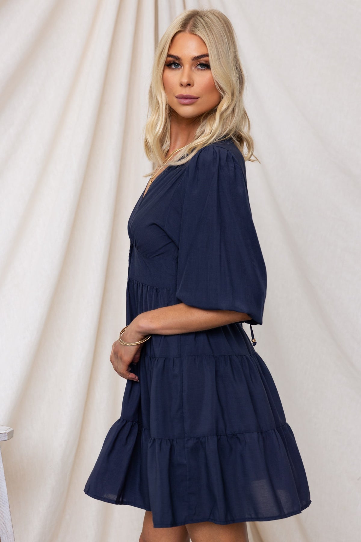 Side view of a model wearing the Damika Dress, a navy chiffon dress with a V-neckline and drawstring sleeves.