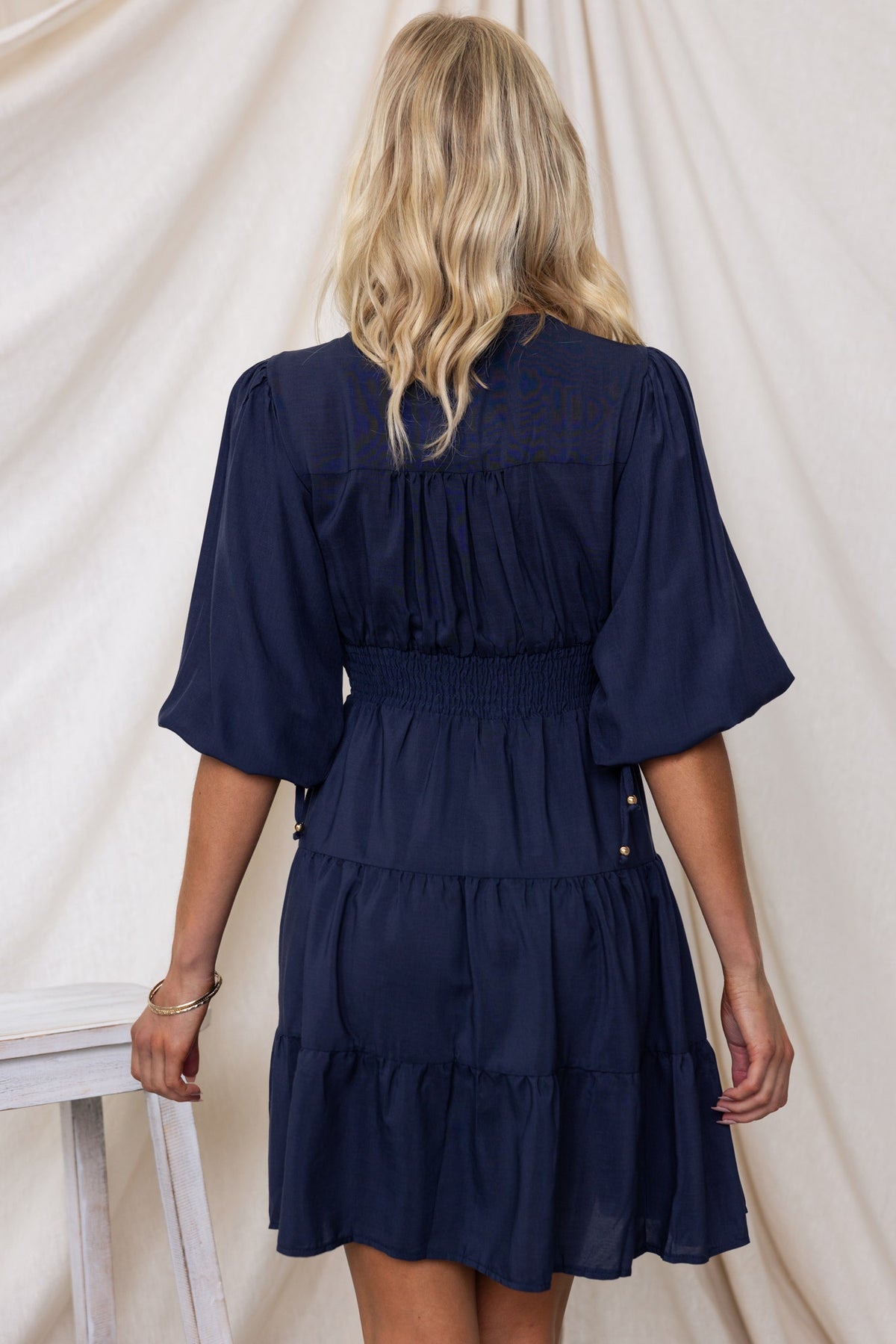 Back view of the Damika Dress in navy, featuring tiered design, smocked waist, and flutter sleeves.
