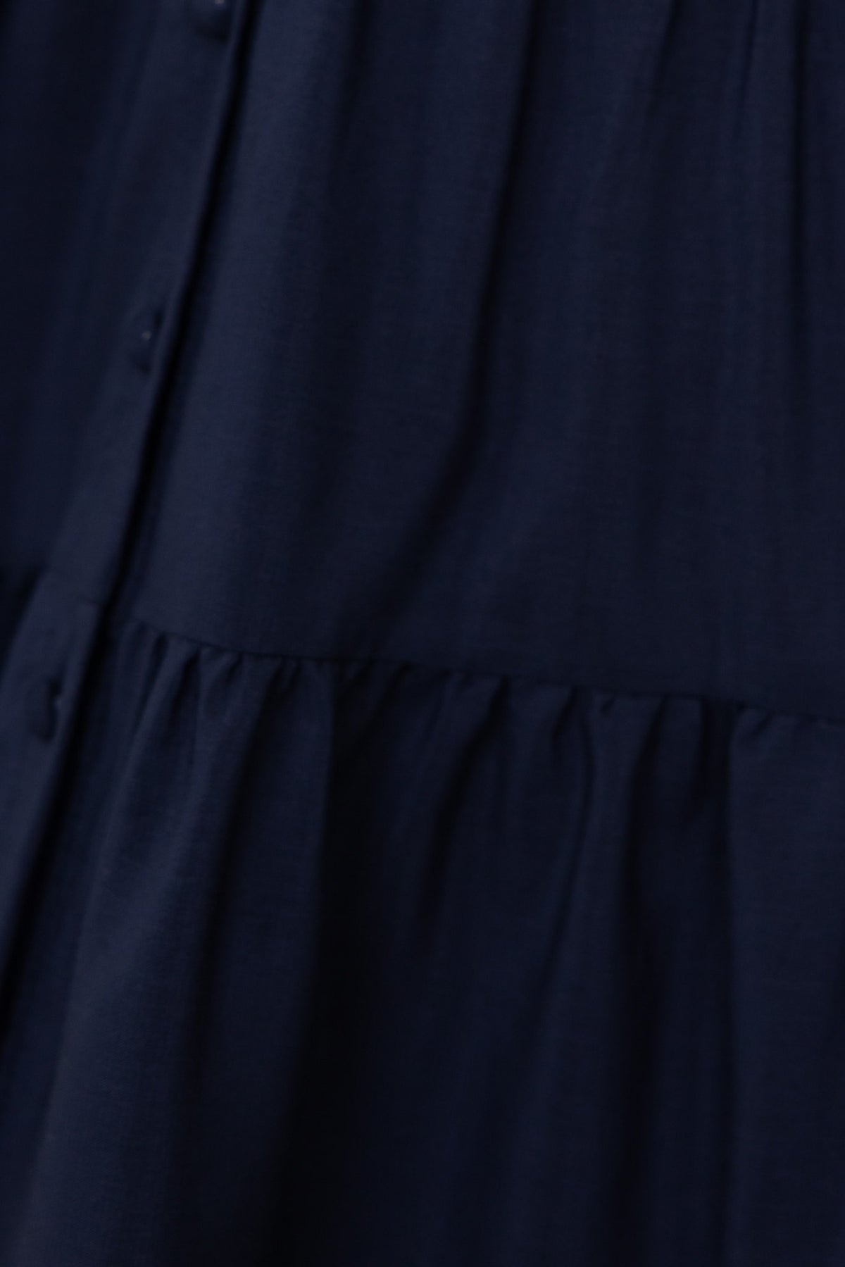 Close-up of navy chiffon fabric with button front and gathered tiered detail from the Damika Dress.