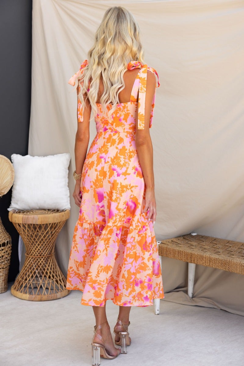 Back view of a floral print Gratified Midi Dress with adjustable tie straps and tiered hem, worn by a woman with long hair.