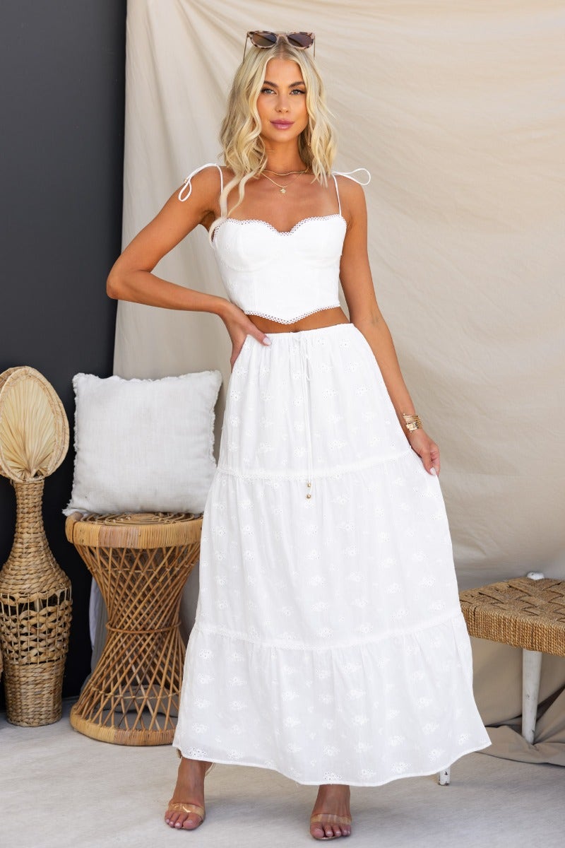 Model wearing a white corset style top with adjustable straps, paired with a flowy maxi skirt in a stylish summer setting.