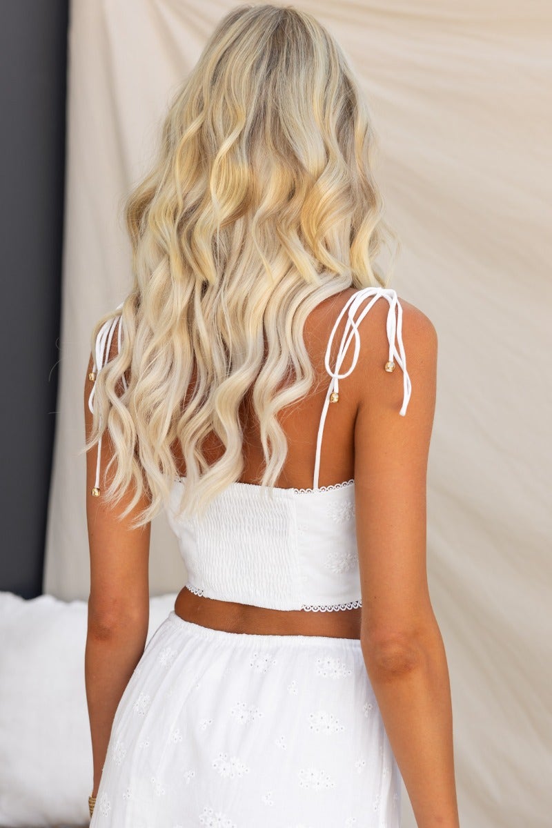 Back view of a woman wearing a corset style white top with adjustable straps and styled wavy blonde hair.