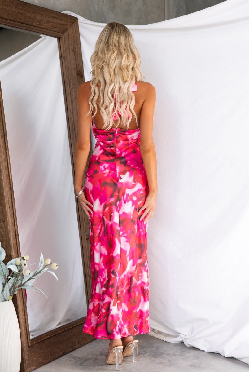 Back view of a woman in a floral satin maxi dress with adjustable halter neckline, styled elegantly near a mirror.