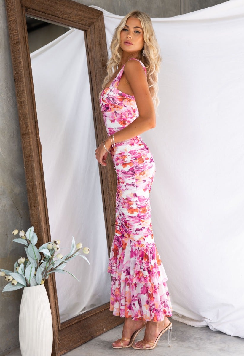 Rosetta Maxi Dress featuring a floral mesh overlay and ruffle hem, modeled by a woman with wavy hair in a stylish setting.