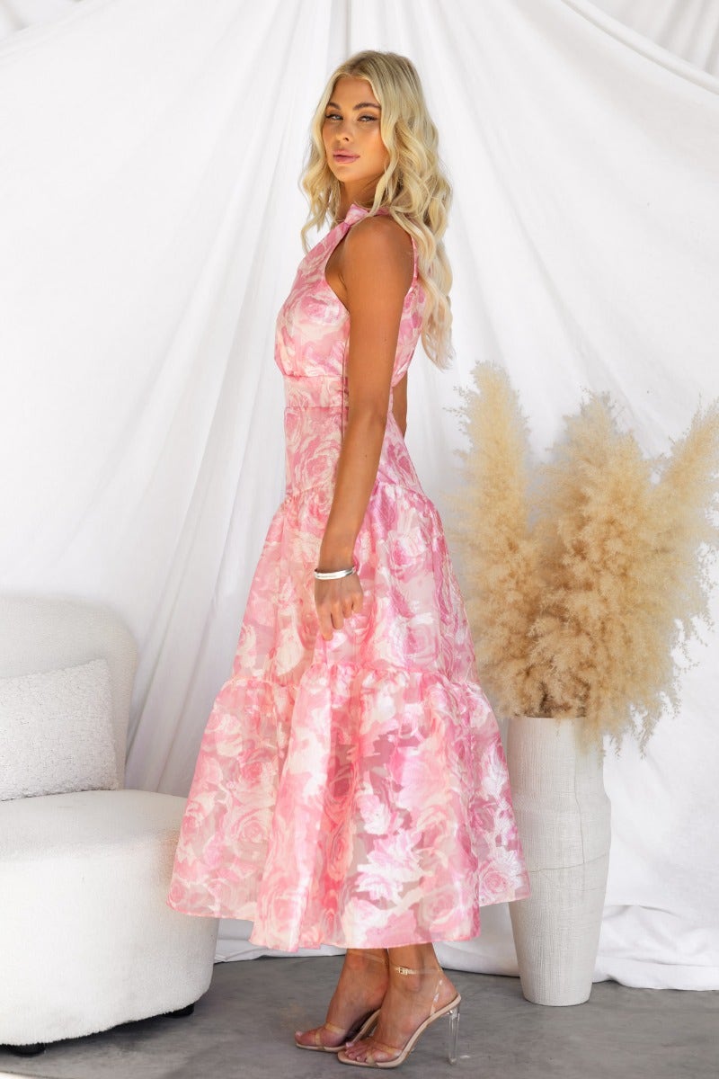 Model wearing a pink floral print maxi dress with one-shoulder neckline, styled with clear heels.