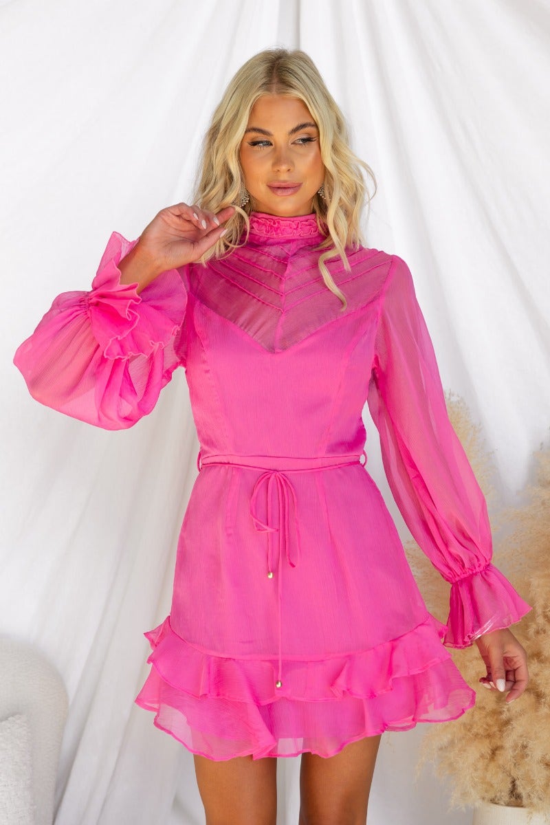 Bright pink chiffon Encore Dress with high neckline, long sleeves, and ruffled hem, styled by model.