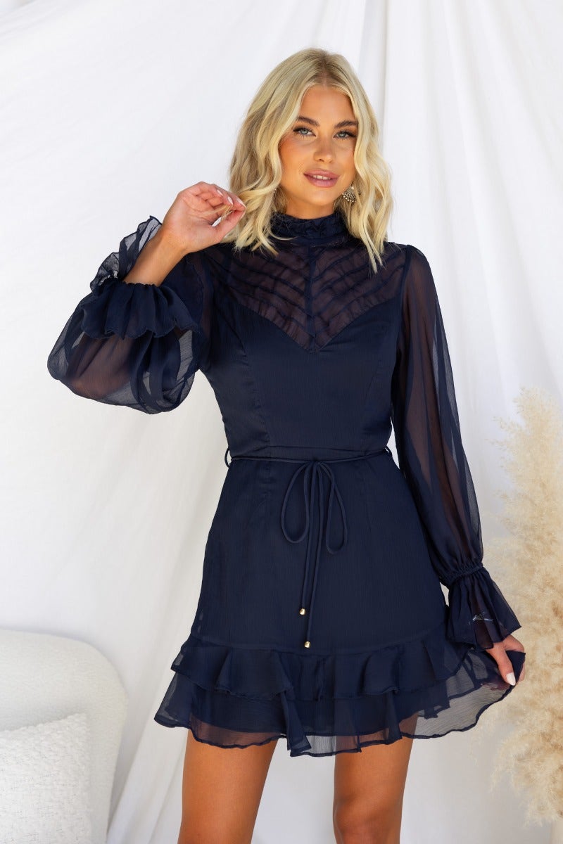 Model wearing a navy chiffon Encore Dress with high neckline, elastic sleeves, and removable fabric tie.
