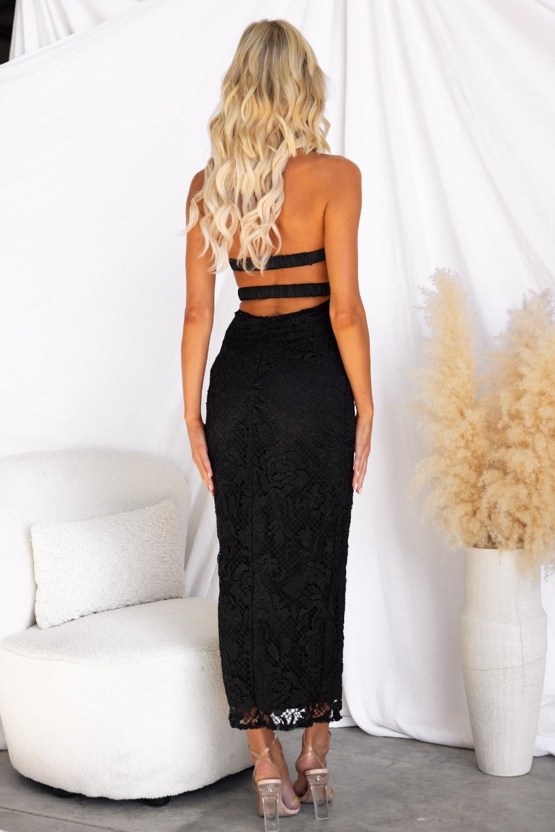 Rear view of a model wearing a black lace strapless midi dress with a fitted silhouette and back straps.