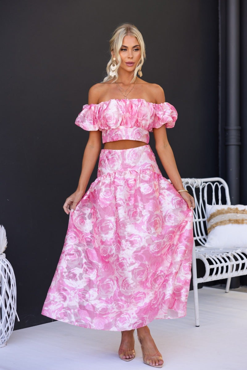 Model wearing a floral print off-shoulder top and maxi skirt set in pink with ruffled sleeves.