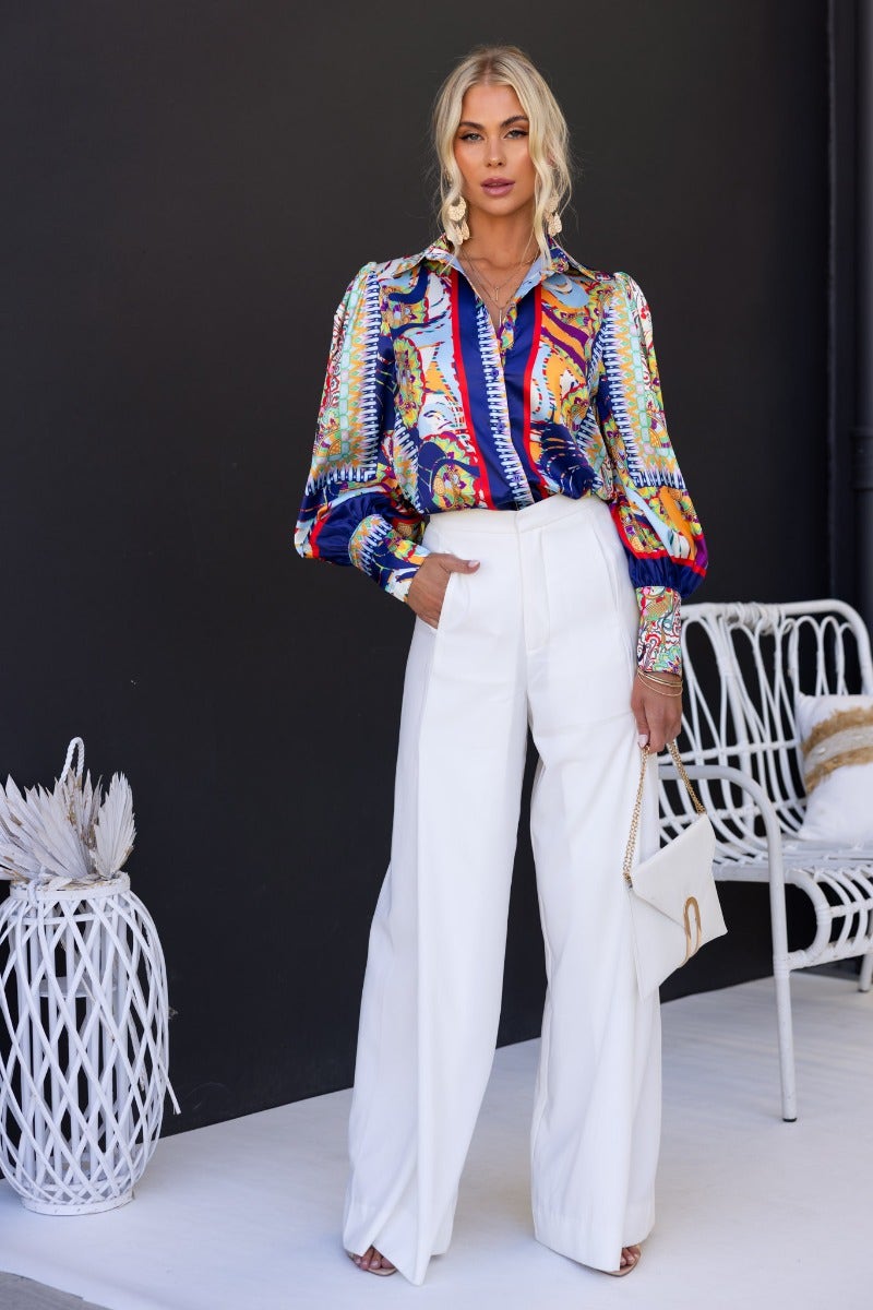 Model wearing Indianna Shirt, a colorful print button-up, paired with white wide-leg trousers.