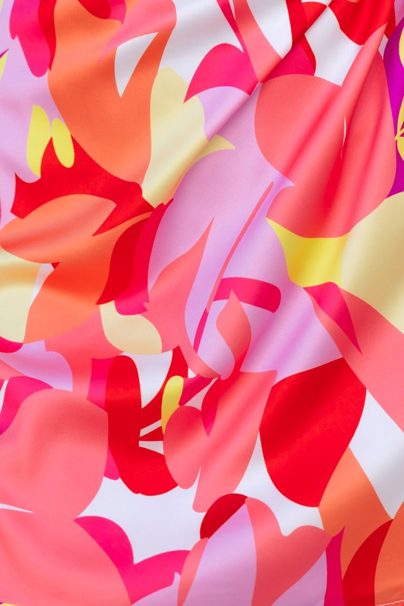 Close-up of vibrant satin fabric featuring a colorful floral pattern in shades of pink, orange, and yellow.