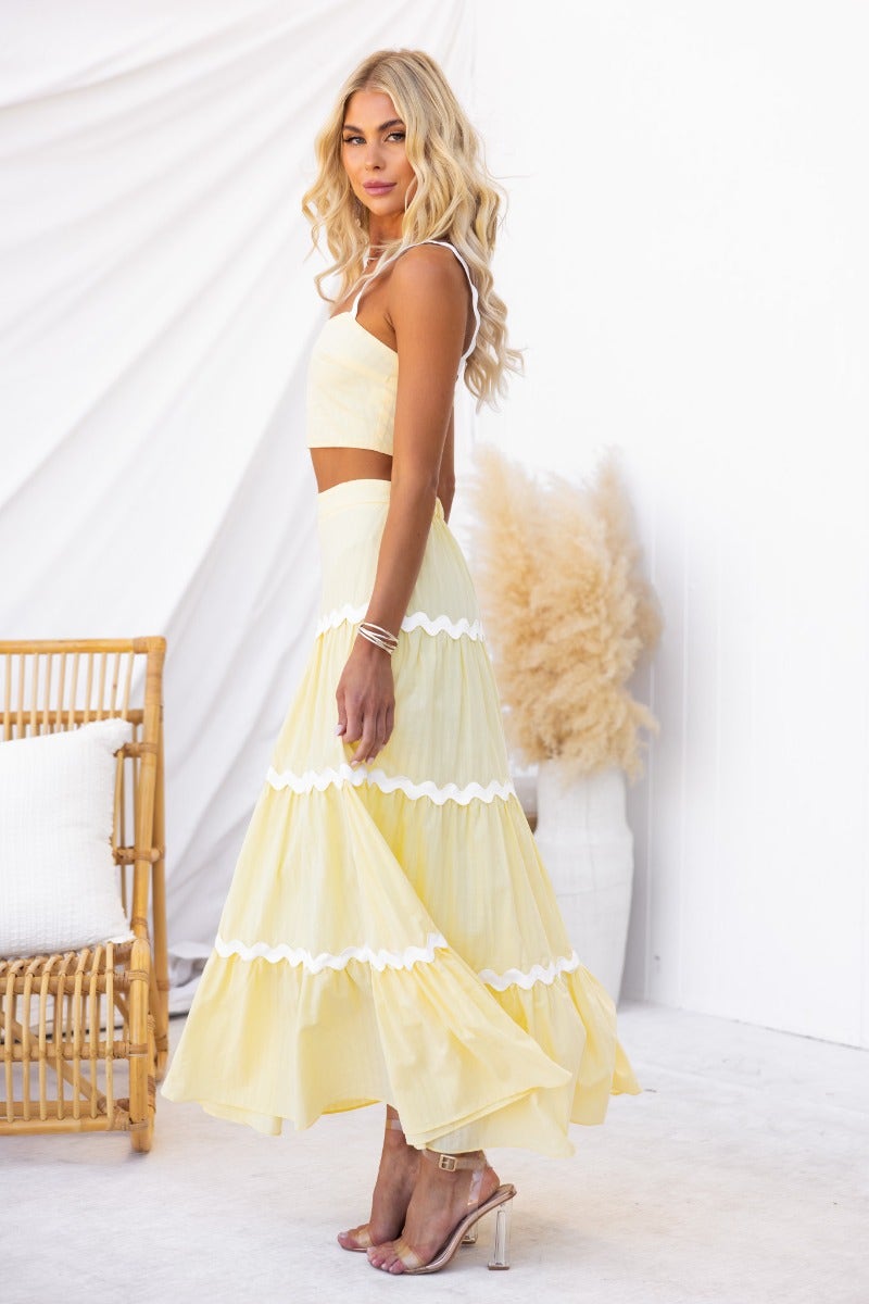 Model wearing a breezy yellow cotton set featuring a crop top and a lined maxi skirt with white trim.