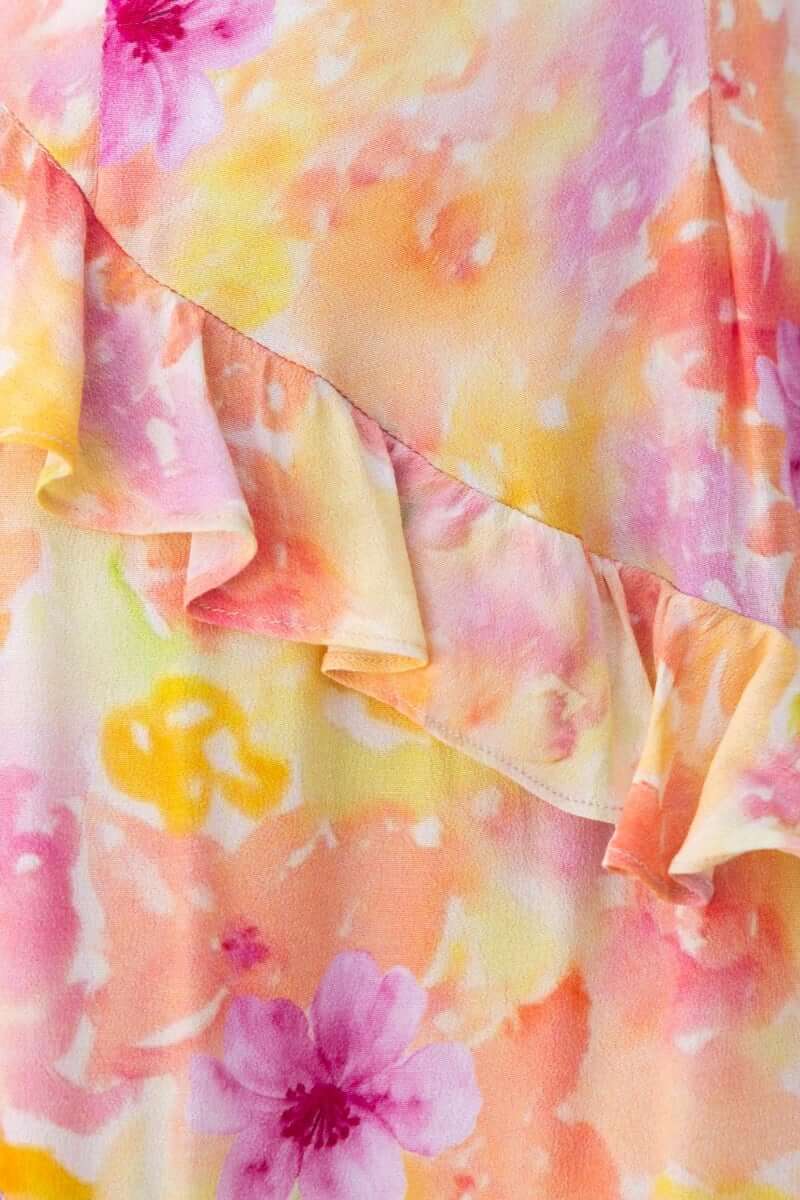 Close-up of floral print fabric featuring ruffle detailing in soft orange and pink hues.