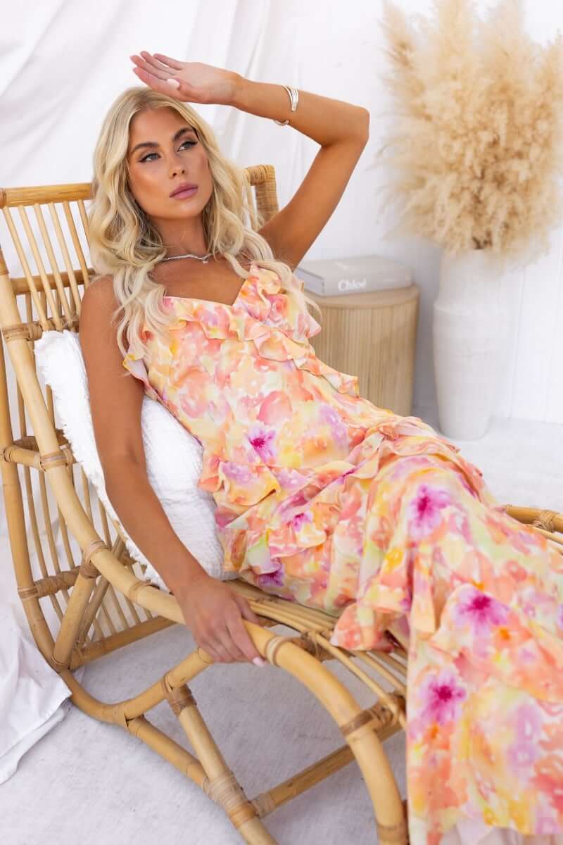 Woman lounging in a floral print Aquarius maxi dress with ruffle detailing, styled in a boho setting.