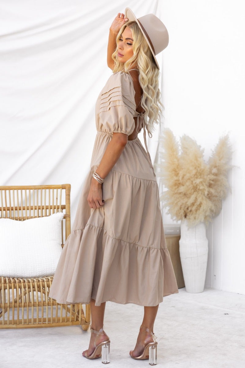 Side view of a model wearing the Oteo Midi Dress in light beige, featuring a boat neckline and tiered skirt.
