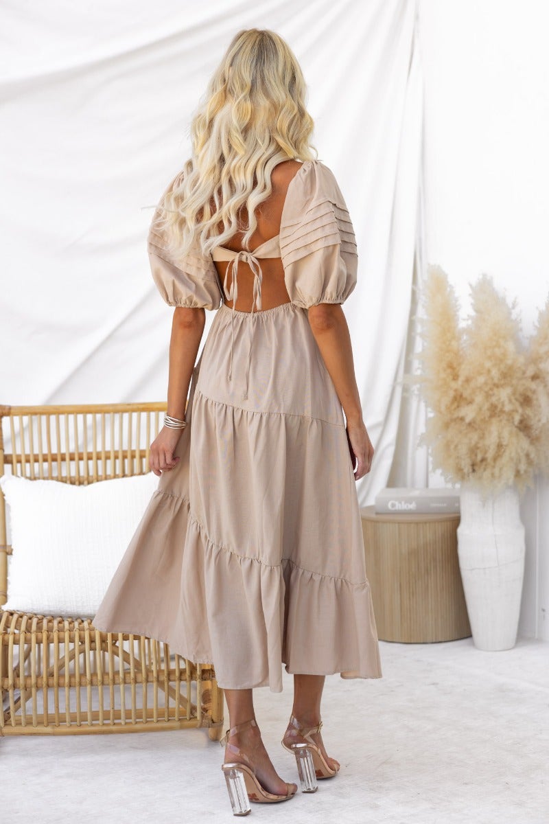 Oteo Midi Dress in taupe with boat neckline and gathered sleeves, styled with strappy heels against a bright background.