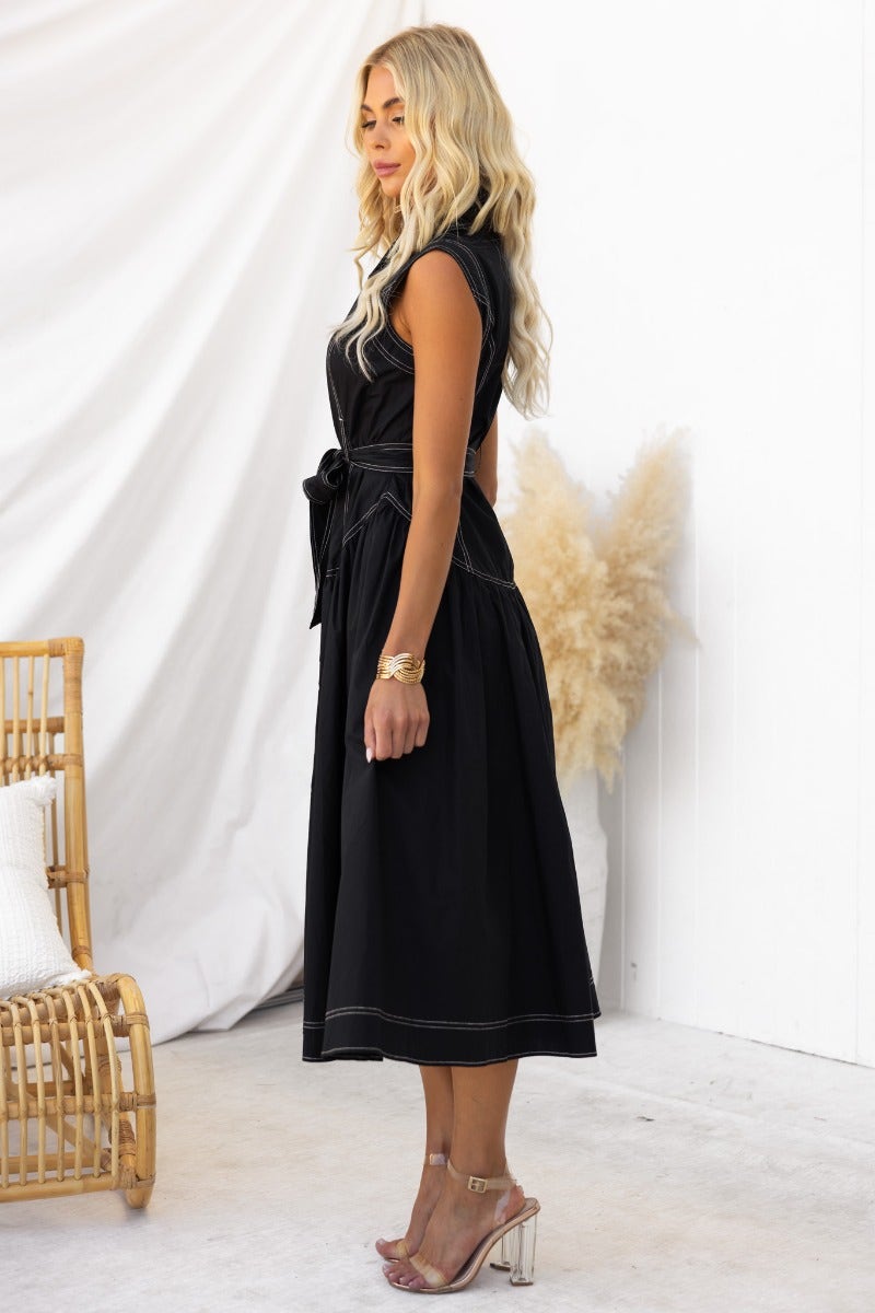 Side view of a model in a black midi dress with a collar, button-up front, and removable tie.