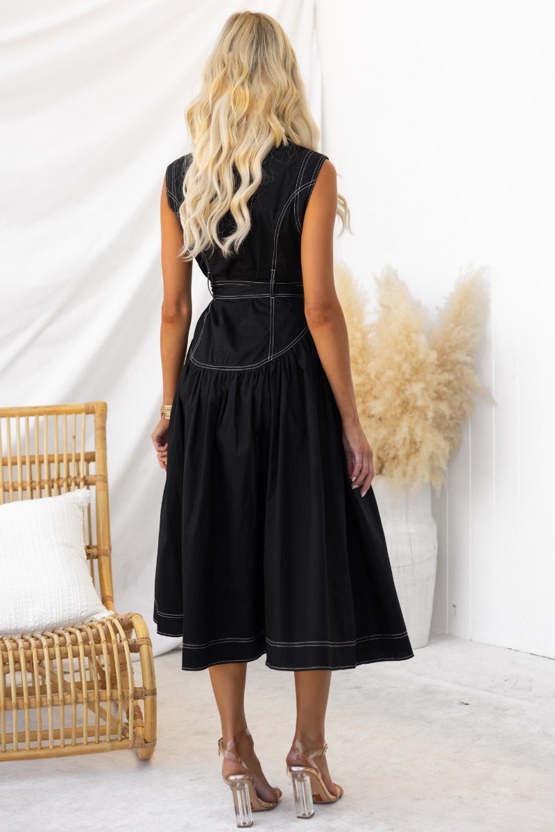 Back view of a woman in a black midi dress with a collar and removable tie, styled with heels.