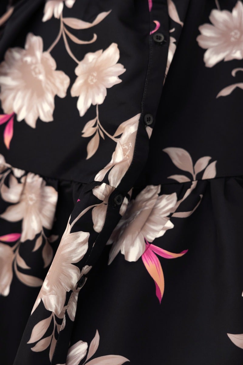 Close-up of black dress with floral print, featuring button detail and relaxed fit, perfect for stylish occasions.