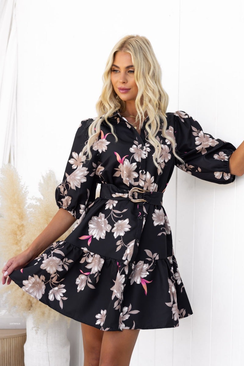 Model wearing a black floral Poise Dress with a collar, button-up front, and removable fabric belt.