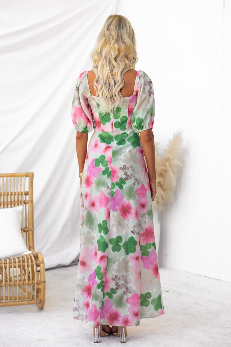 Back view of woman in floral Eyre Maxi Dress with puff sleeves and tie detail, showcasing vibrant pink and green print.