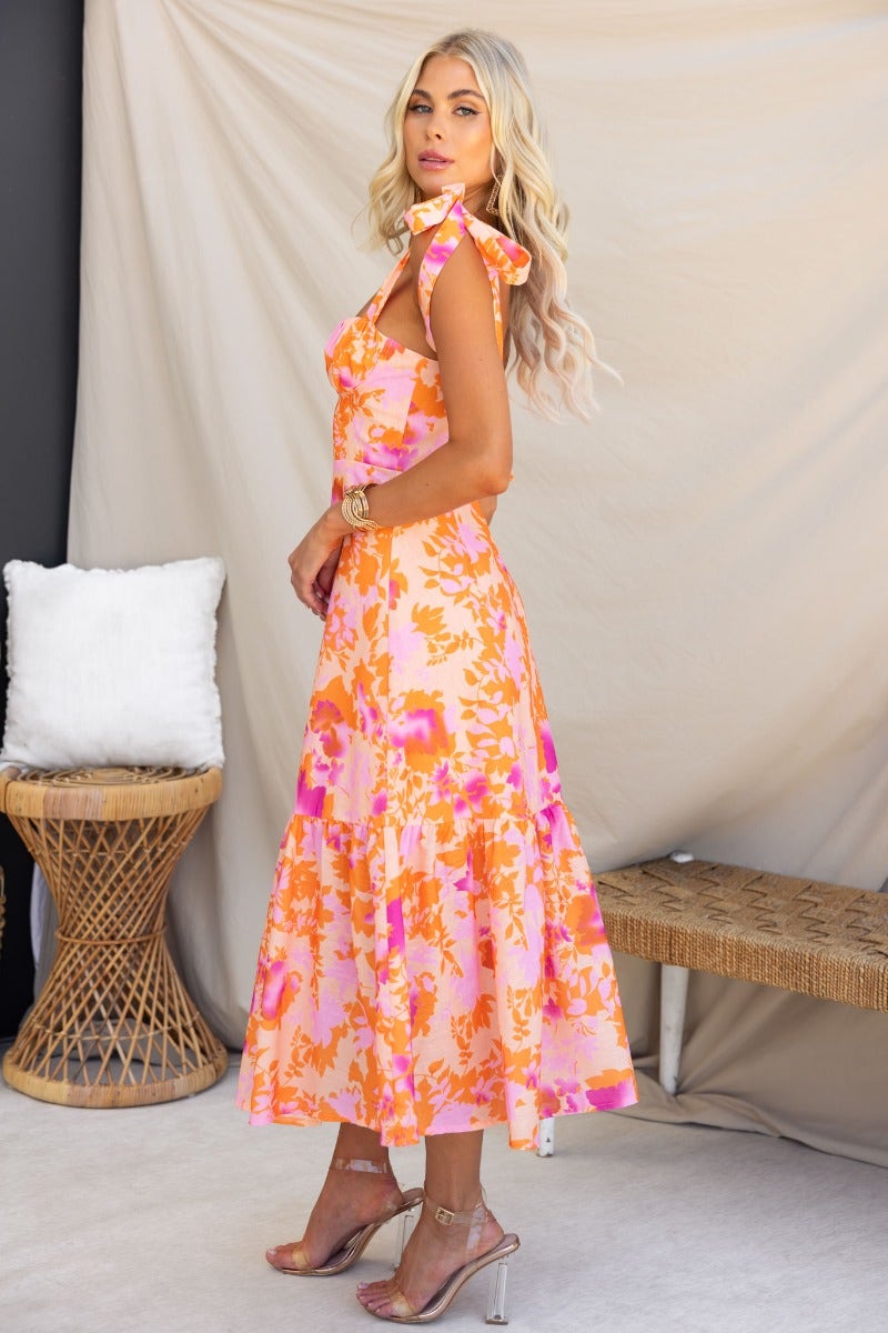 Model wearing the Gratified Midi Dress, a floral print dress with adjustable straps, styled in a bright, summery design.