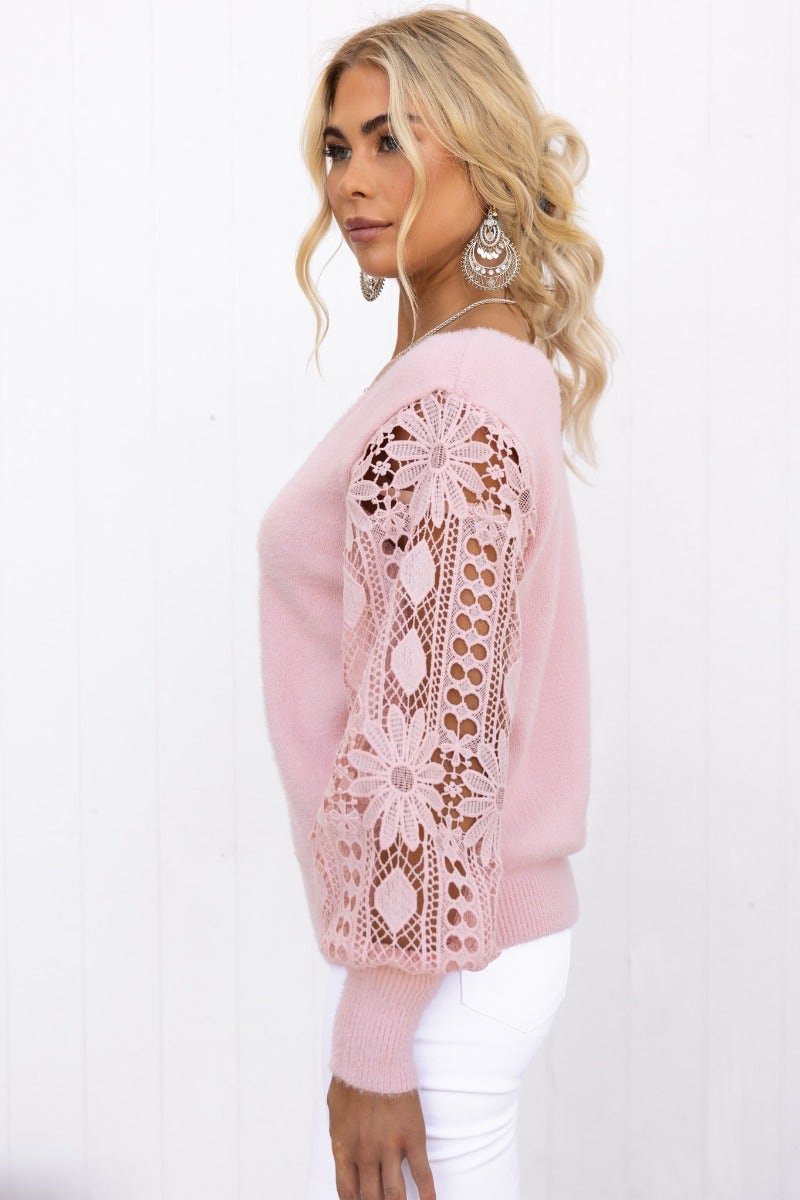 Fluffy pink knit jumper with V-neckline and lace sleeves, styled with white pants and earrings.