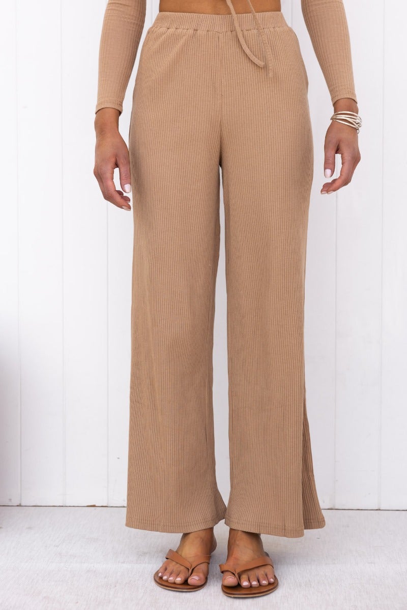 A model wearing Smitten Pants, ribbed knit wide-leg pants in a beige color with an elastic waistband.