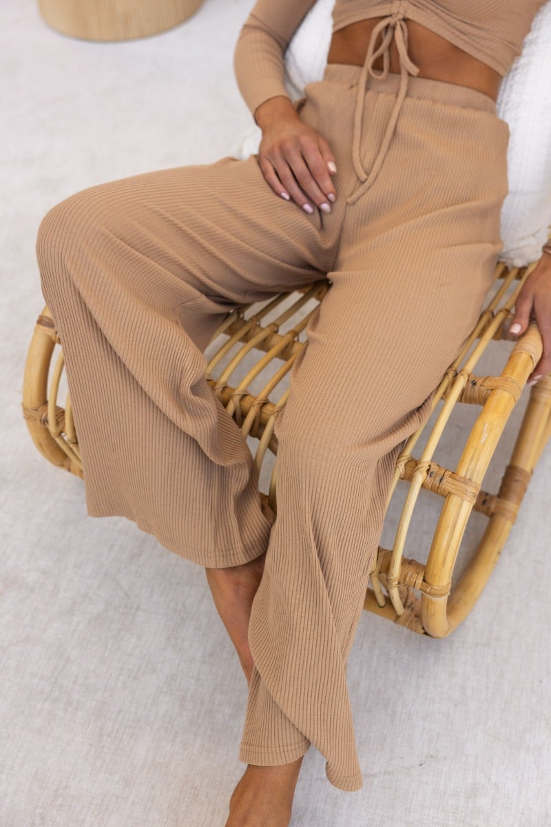 Smitten Pants in ribbed knit, featuring an elastic waistband and wide legs, styled on a woman seated on a rattan chair.