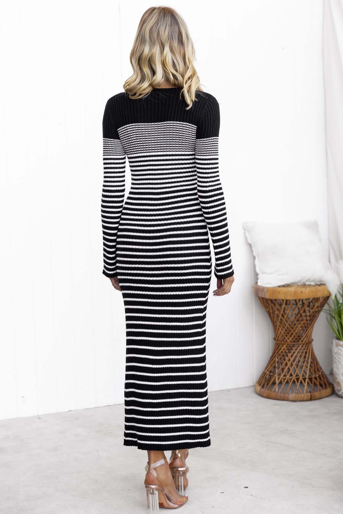 Back view of a striped black and white maxi dress with long sleeves, showcasing its fitted knit design.