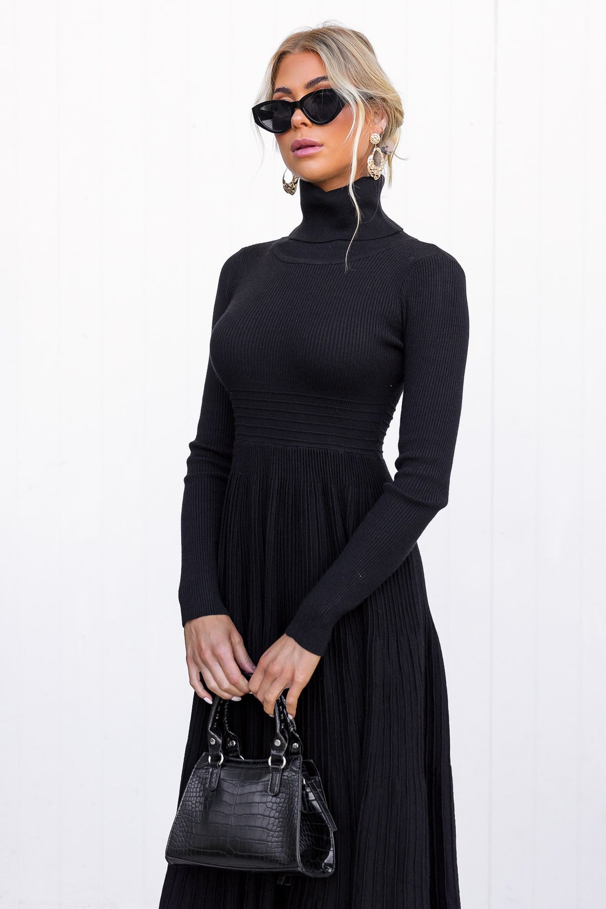 Model wearing a black Parkley midi dress with turtle neckline and ribbed knit material, accessorized with dark sunglasses.