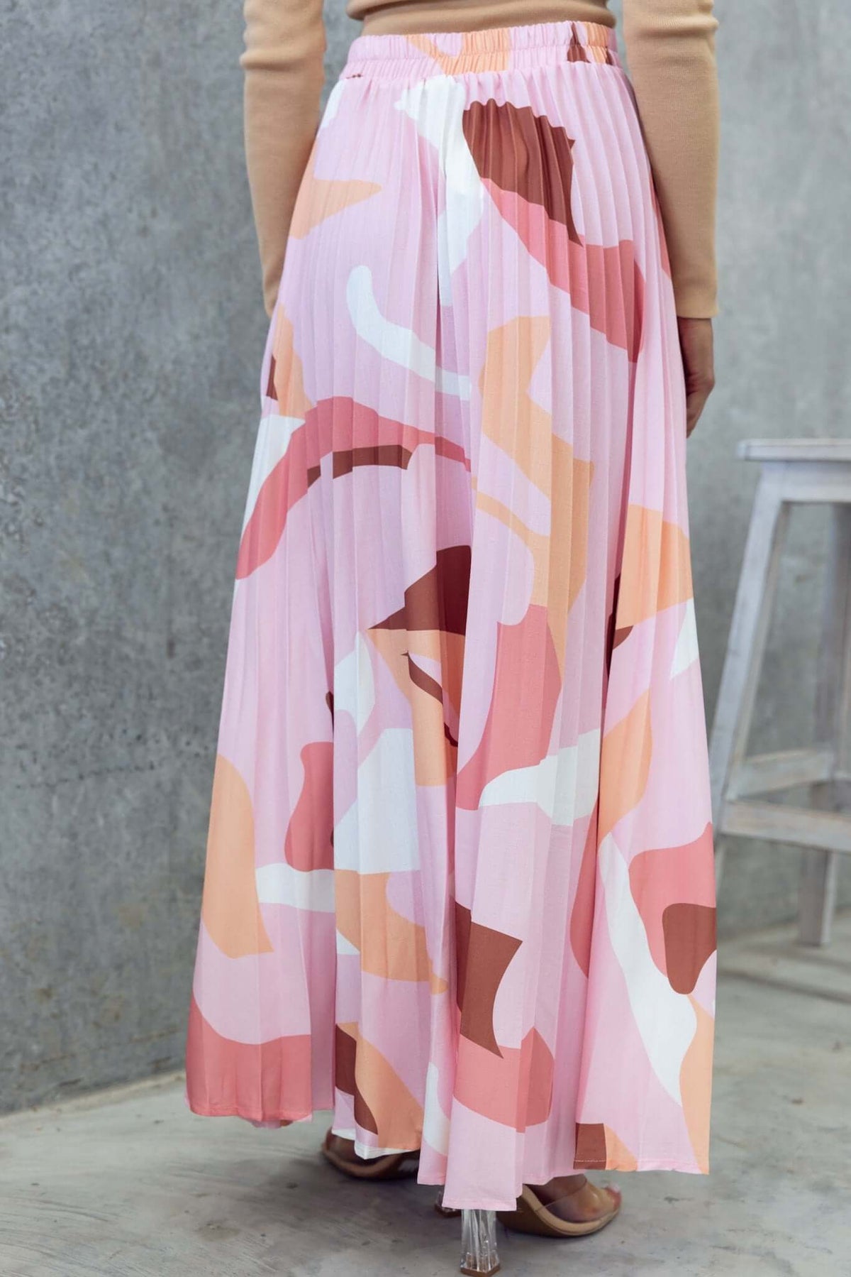 Back view of a pleated maxi skirt in pink and neutral tones, featuring a high waist and elastic band.