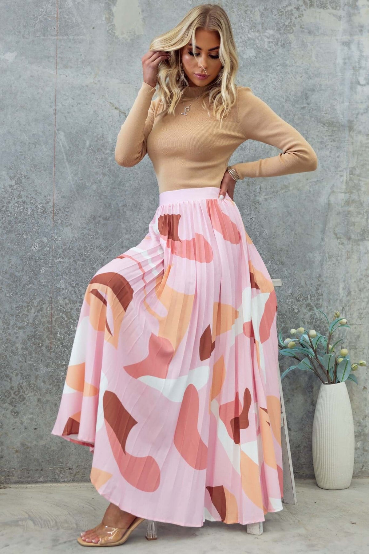 Model wearing a Bankston Maxi Skirt in pink and earthy tones, styled with a fitted top and posing against a textured wall.