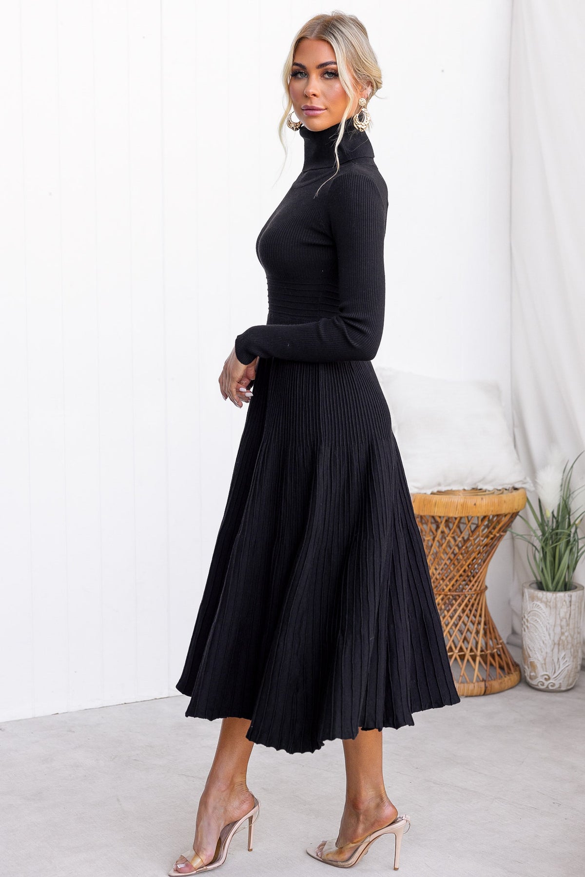 Model in a black Parkley midi dress with turtle neckline, ribbed knit fabric, and pleated skirt.