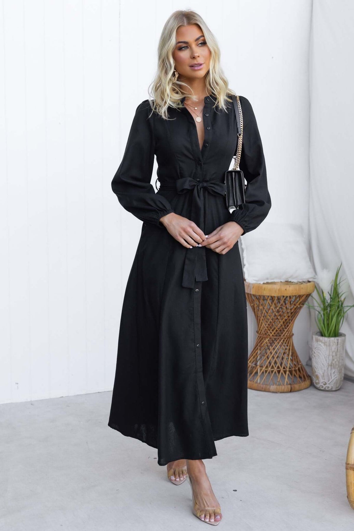 Model wearing a black Delgado maxi dress with button-up front, elastic sleeves, and removable tie.