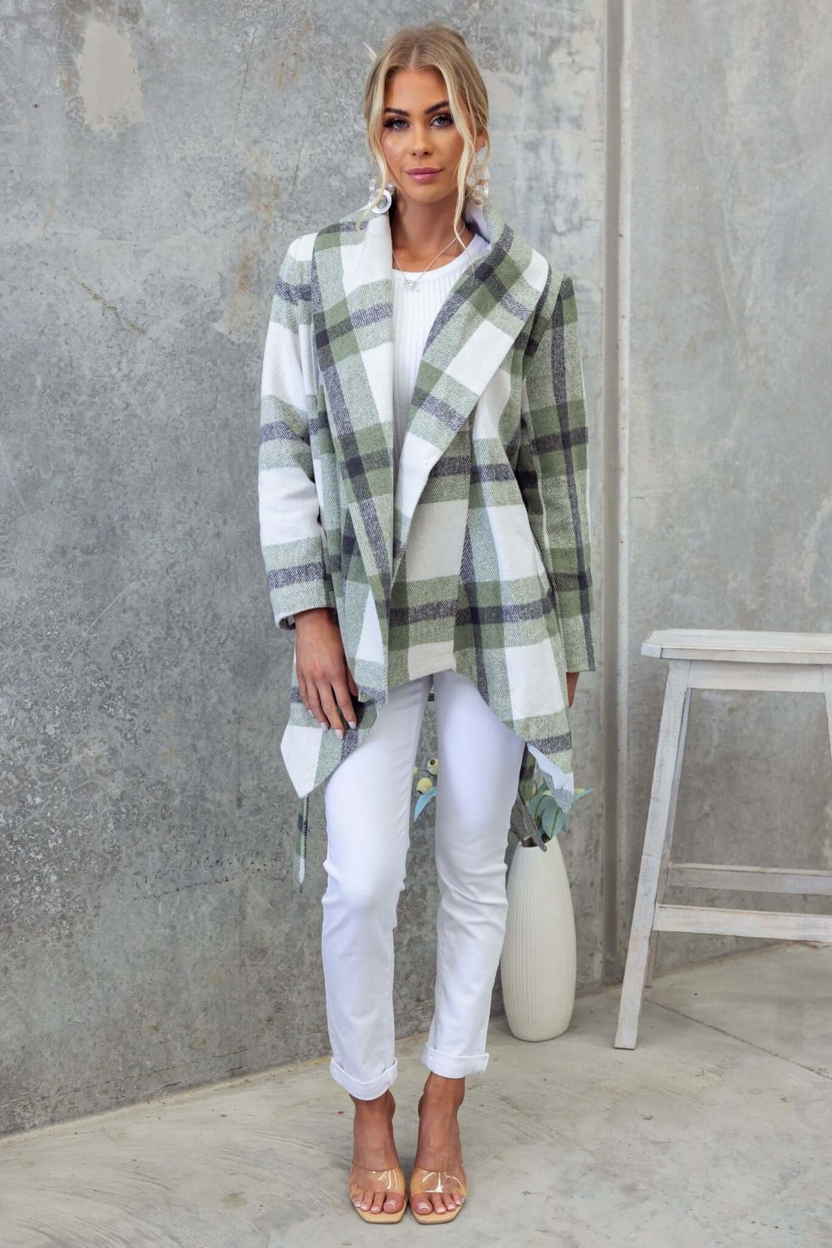Model wearing a stylish Phillips coat with a plaid pattern, paired with white pants and sandals, showcasing its relaxed fit.