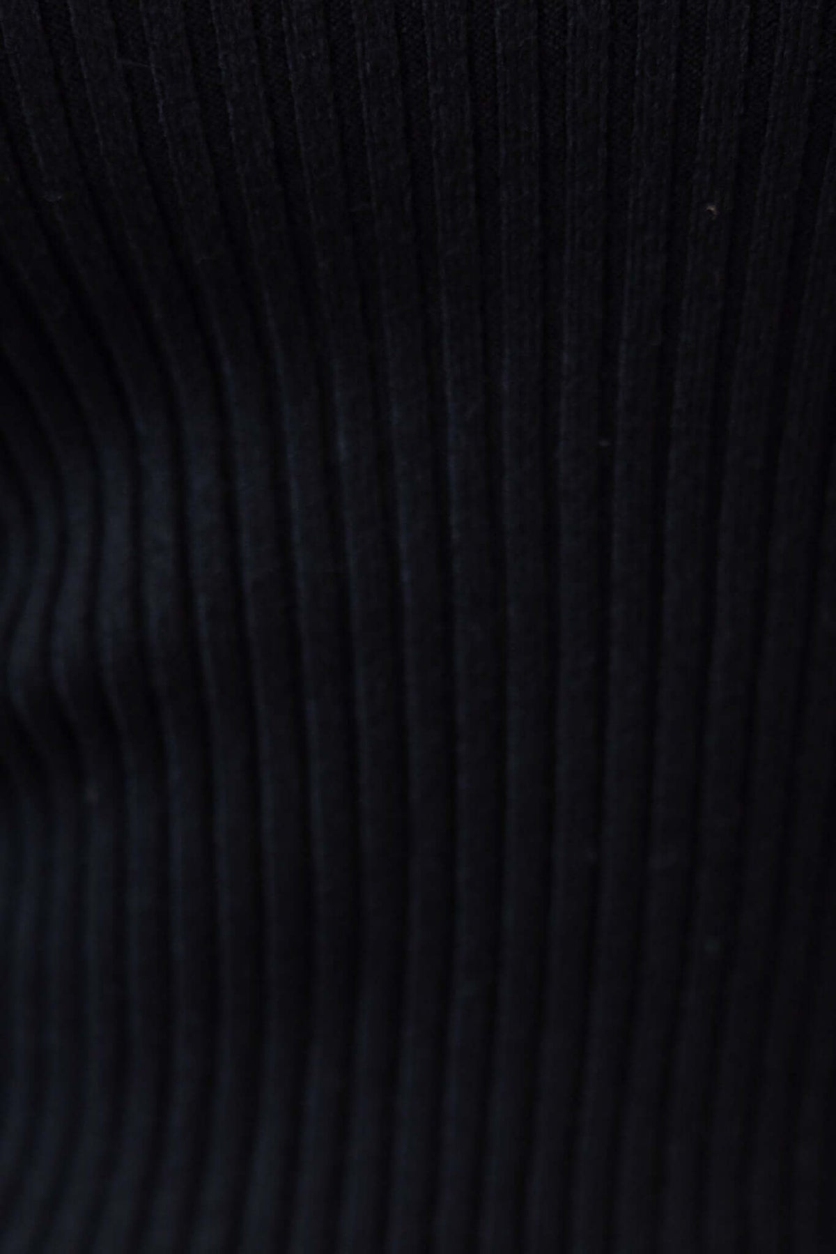 Close-up of ribbed black knit fabric, showcasing its texture and stretch for stylish and comfortable wear.