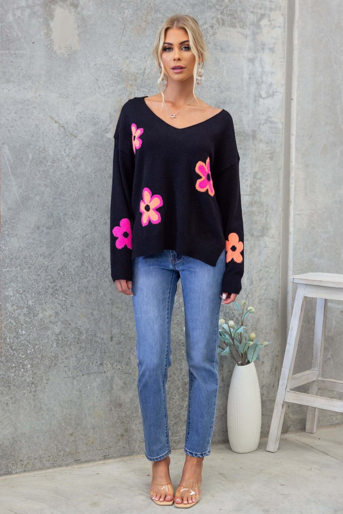 Black Kamen Jumper with floral designs, V-neckline, side splits, paired with blue jeans and sandals.