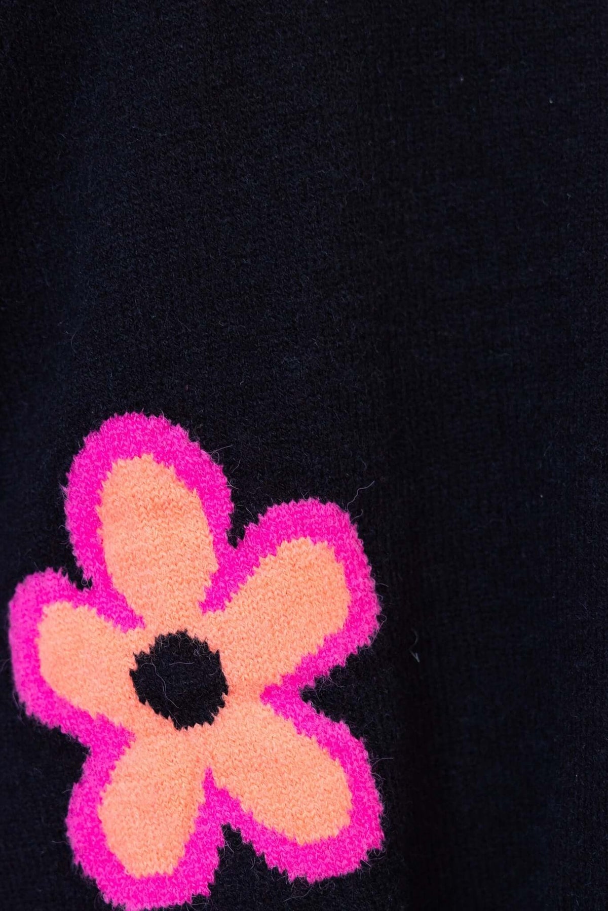 Close-up of a black jumper featuring a vibrant pink and orange flower design on the side.