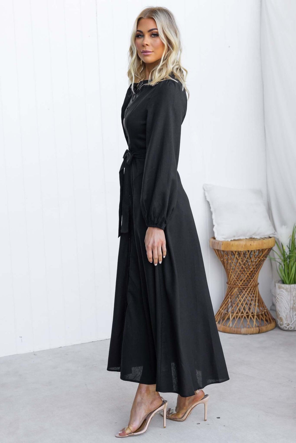 Model wearing a Delgado Maxi Dress, a black button-up dress with a tie, pockets, and linen texture.