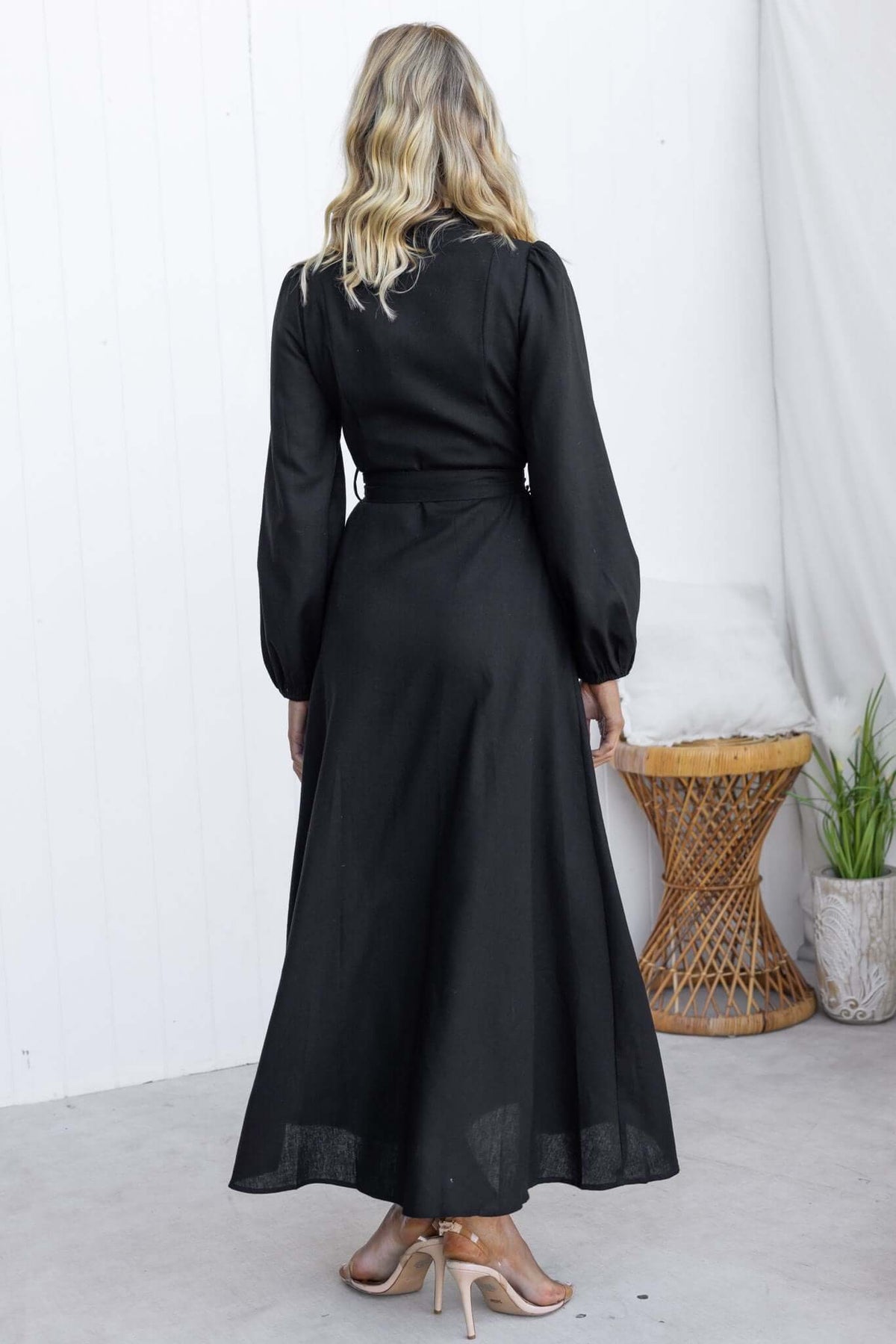 Back view of the Delgado Maxi Dress in black, featuring long sleeves, a removable tie, and a flowing design.
