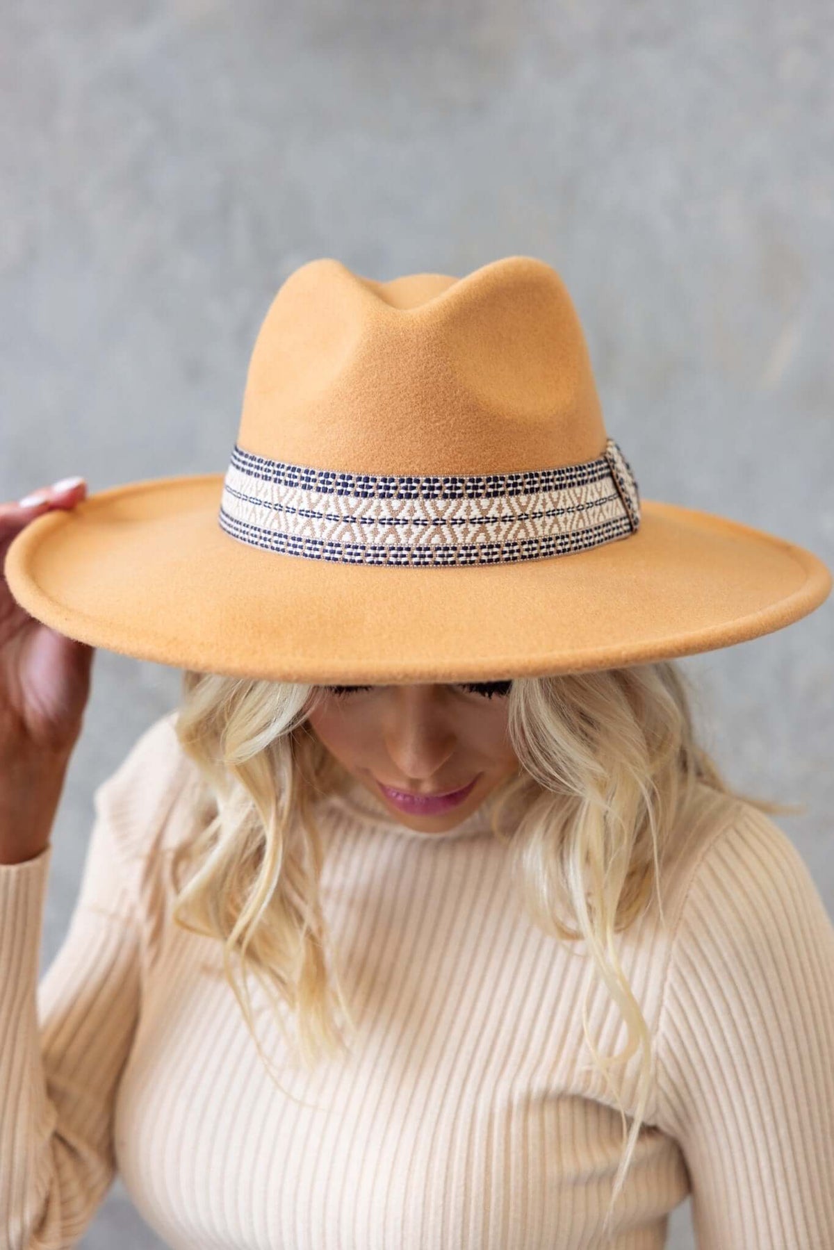 Stylish Kansas hat in tan with a decorative ribbon, worn by a woman outdoors, perfect for fashion and sun protection.