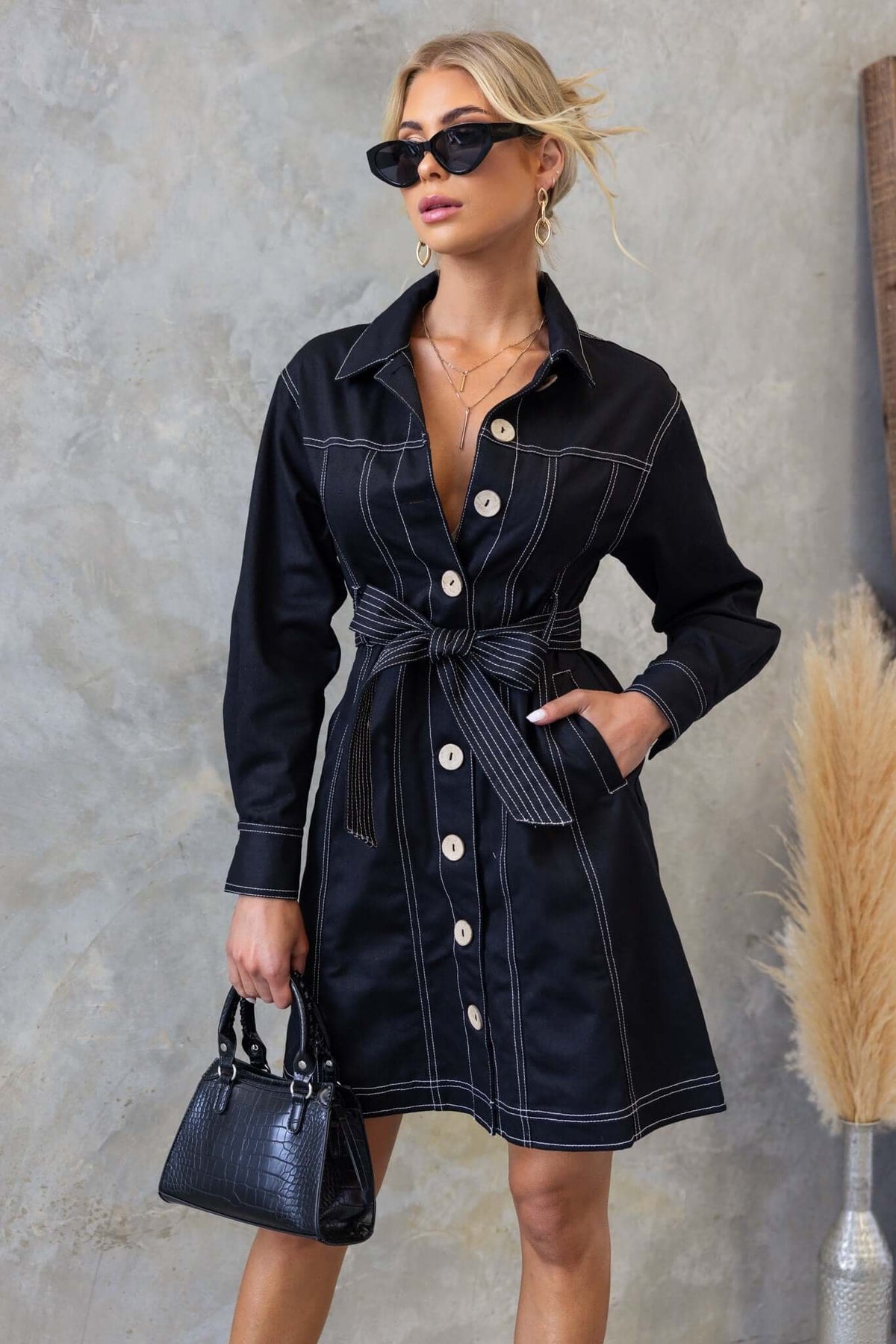 Black denim dress with collar, button-up front, and removable belt, styled with sunglasses and handbag.