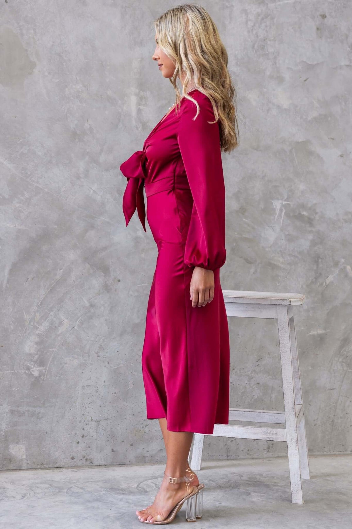 Side view of a woman in a fuchsia satin Cremona Midi Dress with tie at bust and elastic sleeves.