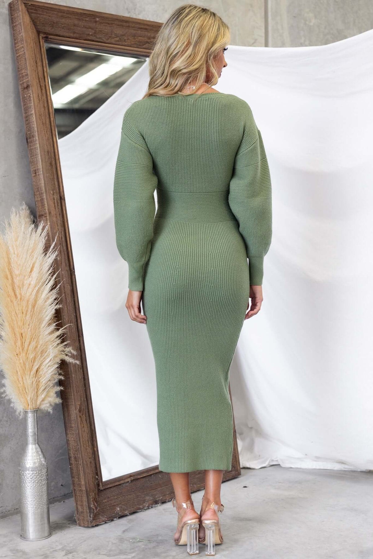 Woman wearing a green ribbed knit maxi dress with a V-neckline, viewed from the back, showcasing its elegant fit.